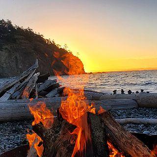 前景是海滩上的一堆火，背景是海洋上的夕阳.