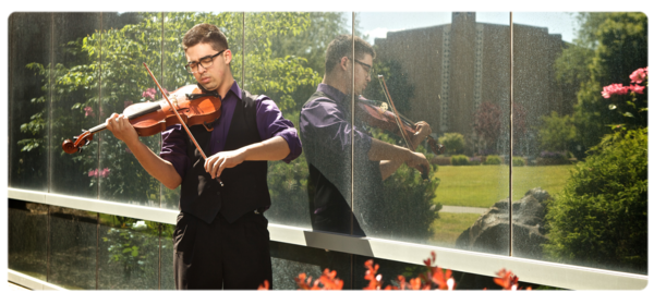 音乐专业的学生在外面拉小提琴，前景是鲜花, 表面反映了大学教堂的背景
